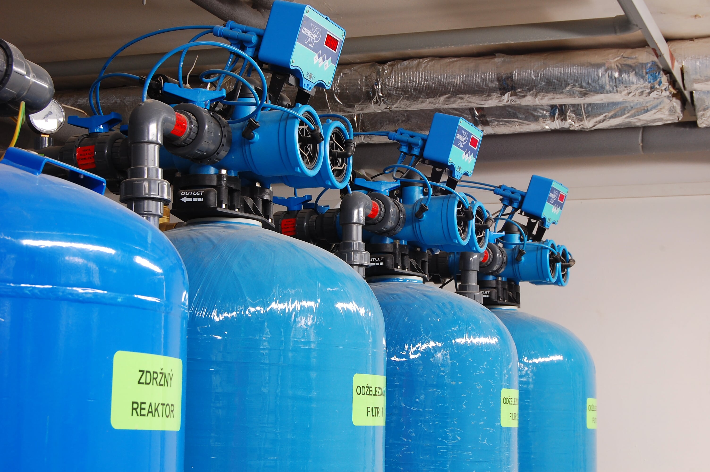 A row of large blue water treatment tanks with control valves in a utility room