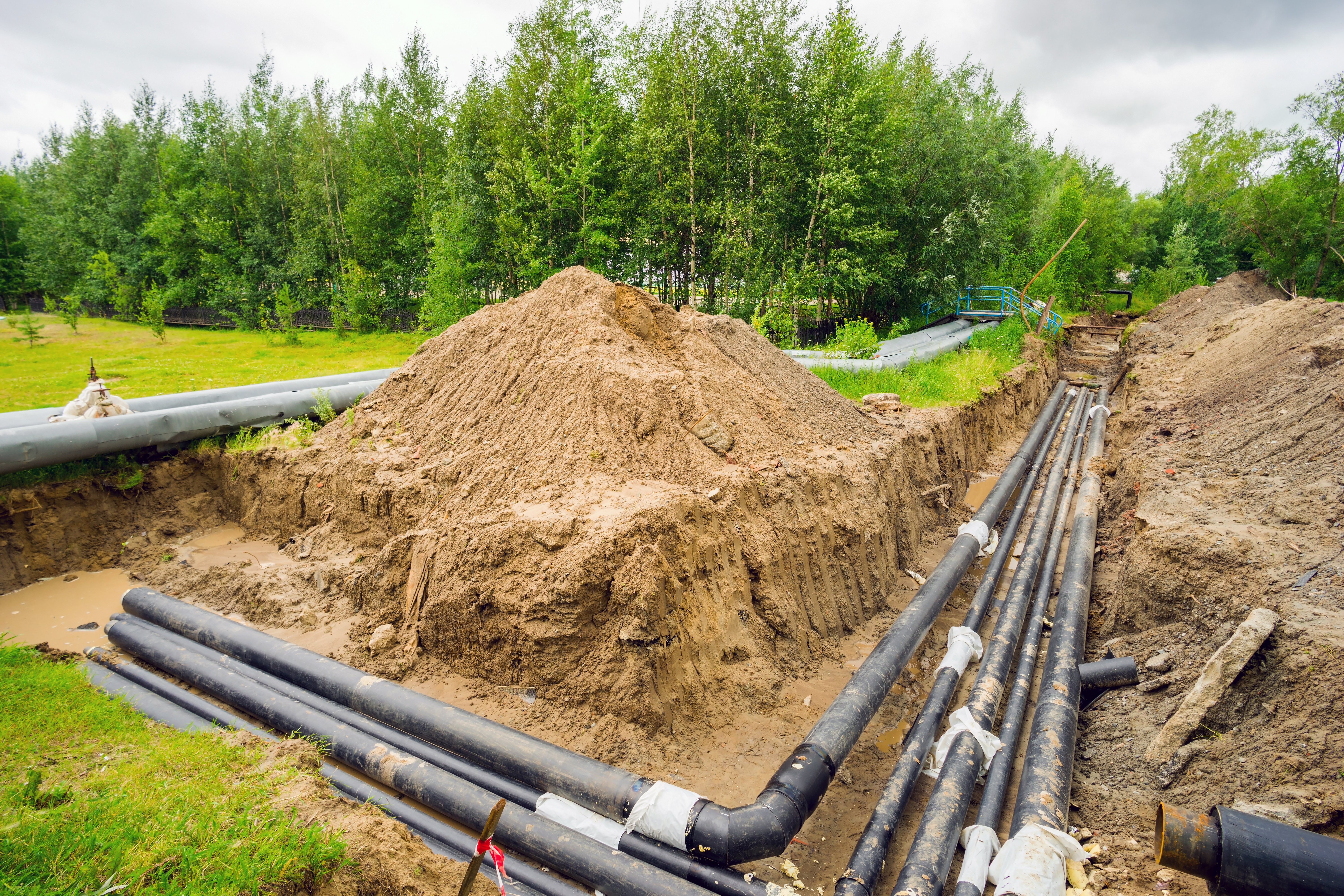 Lengths of pipe laid in an open trench beside a mound of excavated soil