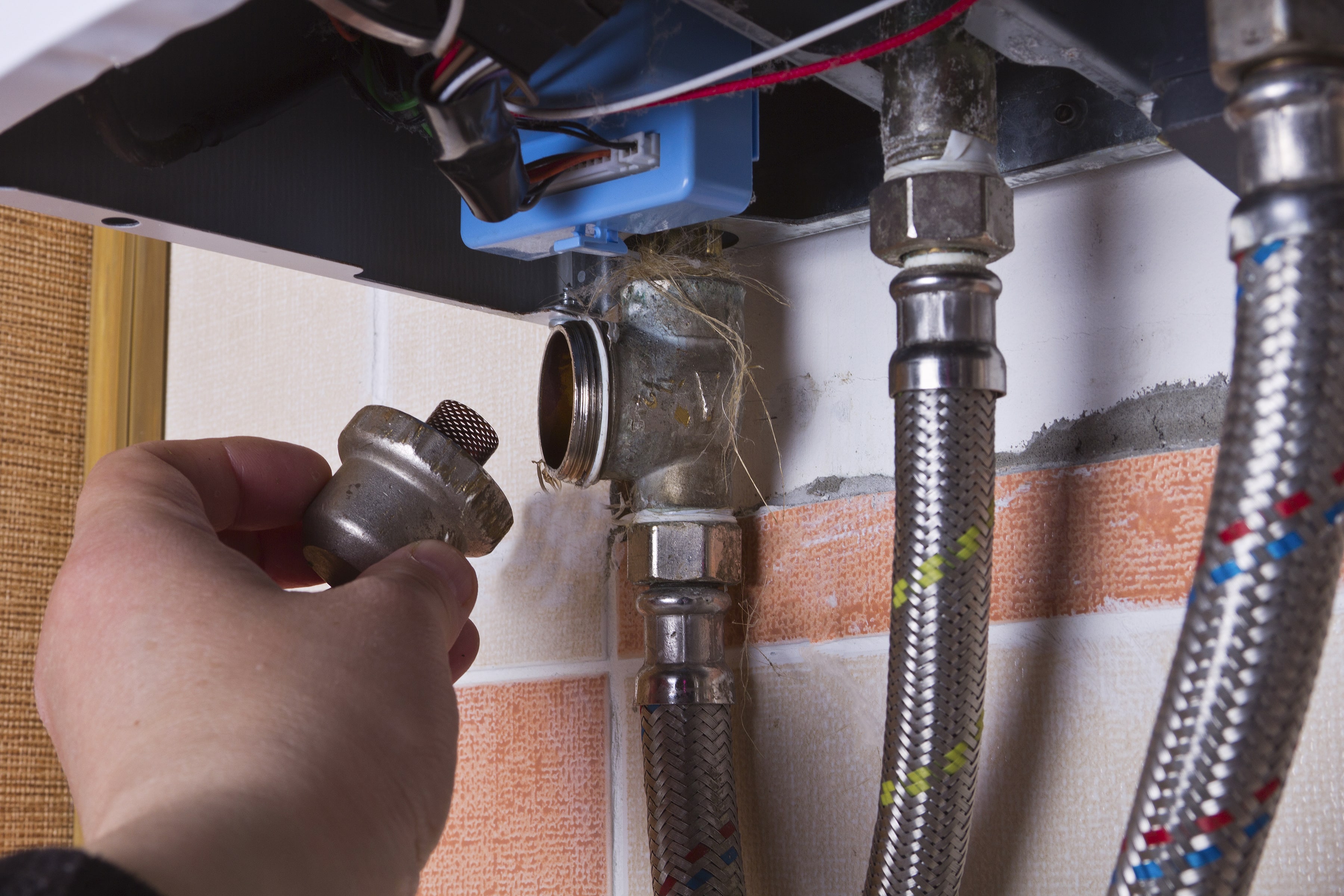 A close-up of a hand fitting a brass connector to water lines beneath a fixture