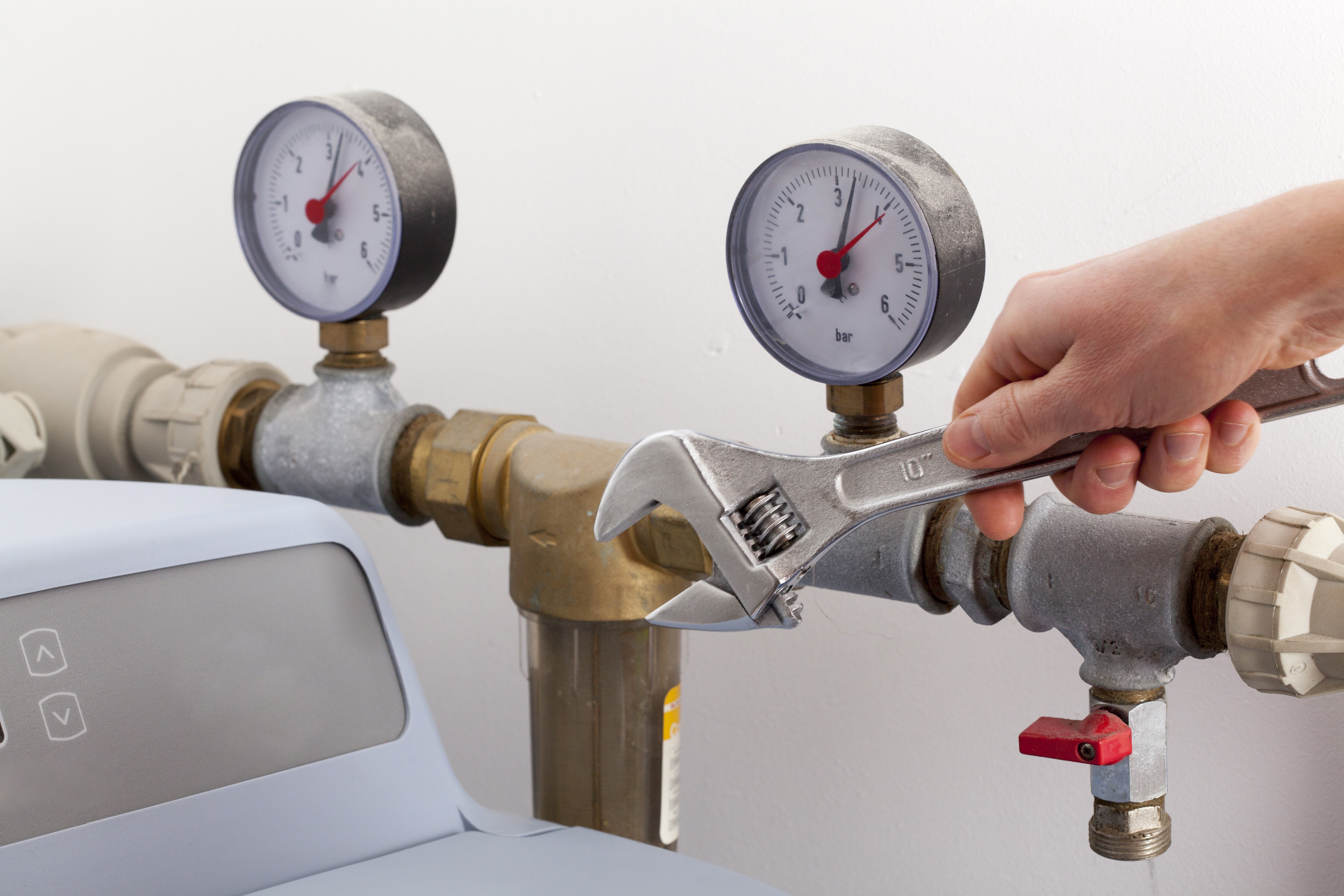 A hand turning an adjustable wrench on a pipe assembly fitted with pressure gauges