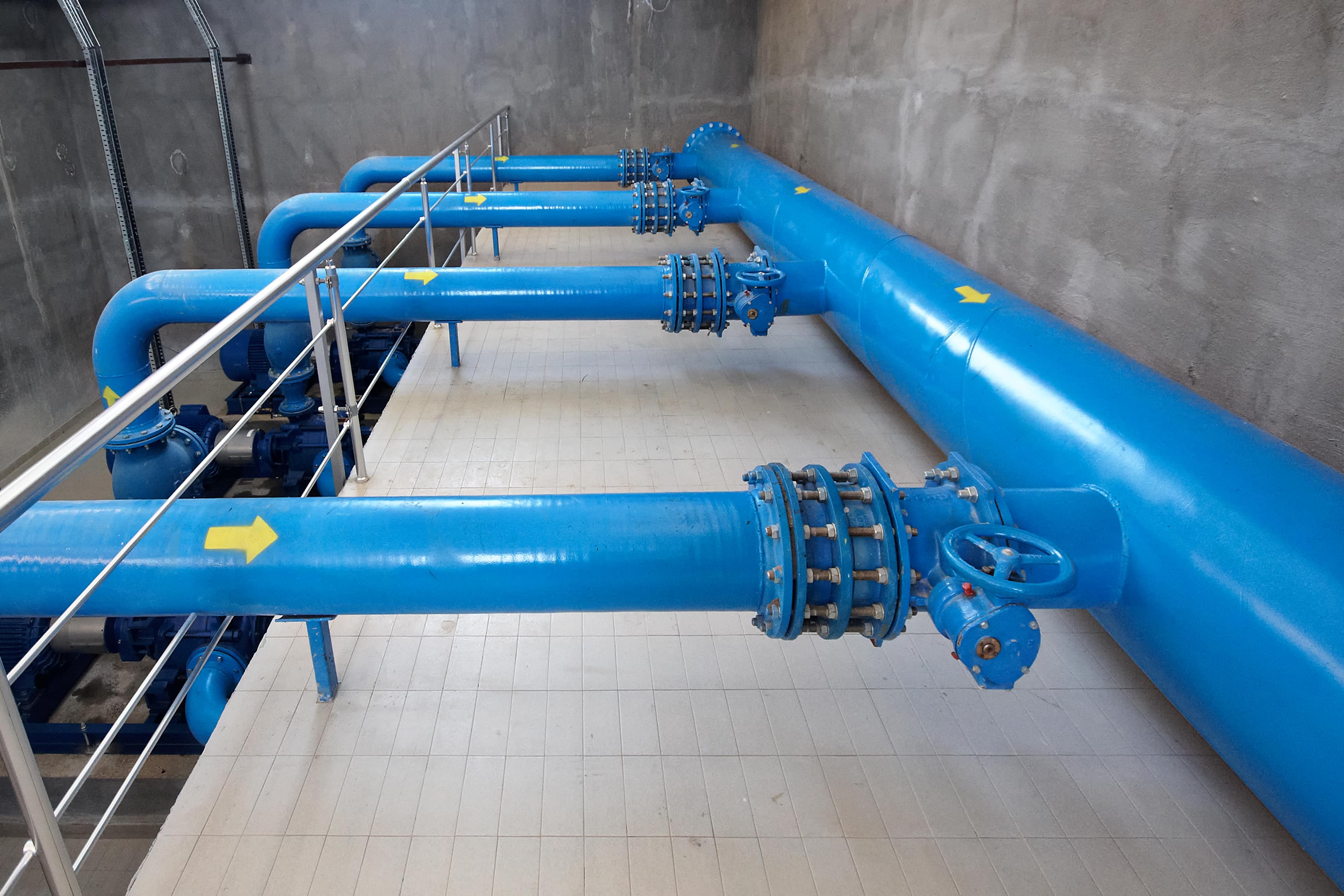Large blue water mains with flanged joints and valves running through a utility room